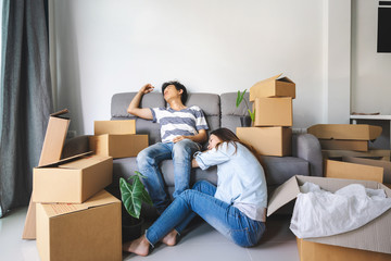 Young tried couple moving in new home, sitting and relaxing on sofa with cardboard boxes