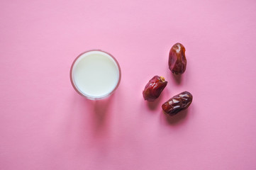 Dry tasty dates and milk on pink background.