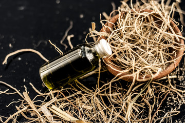 Floral and ayurvedic essence of herb Vetiver grass or Khus in a transparent bottle used in many beverages of Indian and Asia with dried vetiver grass in a clay bowl on black surface.;