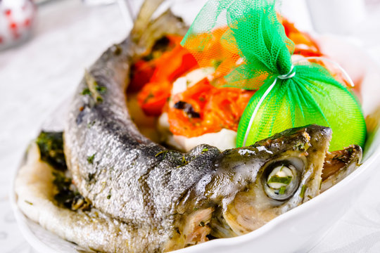 Grilled whole salmon with vegetables on white plate