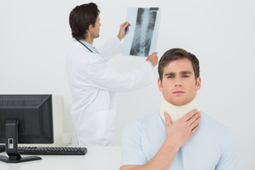 Patient in surgical collar while doctor examining spine xray behind