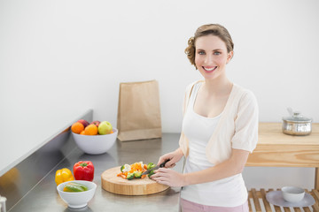 Obraz na płótnie Canvas Cute woman cutting vegetables standing in her kitchen