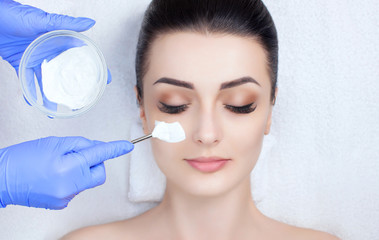 The cosmetologist for the procedure of cleansing and moisturizing the skin, applying a mask with stick to the face of a woman in beauty salon. Cosmetology and professional skin care.