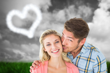 Obraz premium Handsome man kissing girlfriend on cheek against green grass under grey sky
