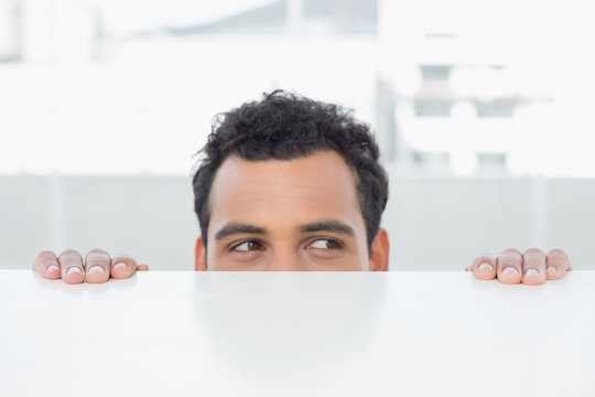 Businessman peeking behind the desk at office - Powered by Adobe