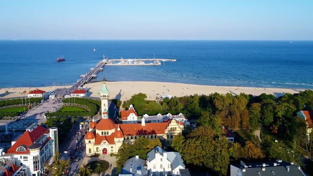 Sopot resort in Poland. Vacation infrastructure with spa, old lighthouse, wooden pier (molo), promenade, marina, yachts, ship and beach. Aerial 4K flyby video in sunset light
