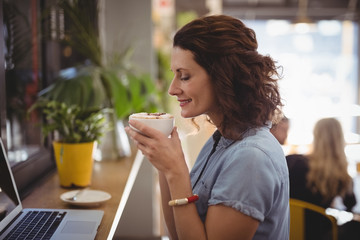 Young woman smelling coffee while sitting at cafe