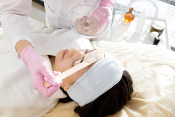 Obraz na płótnie Canvas Close up of female cosmetologist applying facial mask to face of beautiful young woman lying on massage table during beauty treatment in SPA salon