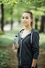 Young woman athlete takes a break, she drinking water, out on a run on a hot day