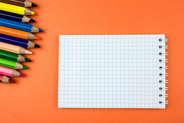 Color pencils, notepad, orange texture. Empty space for text and design. Office tools concept