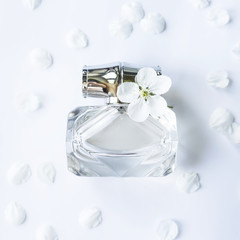 A glass jar of perfume among white spring petals. Women's fragrance