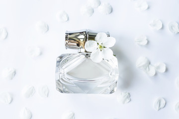 A glass jar of perfume among white spring petals. Women's fragrance