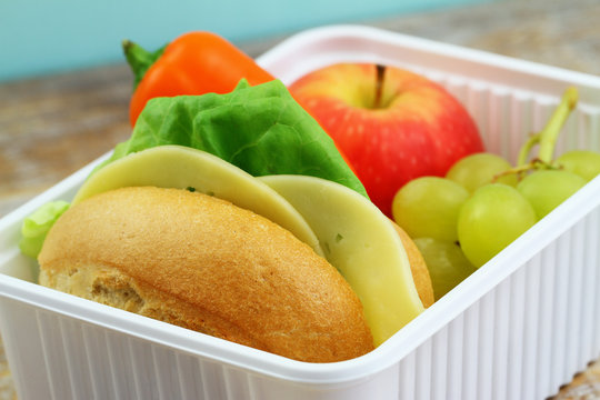 Packed lunch containing cheese roll, crunchy yellow pepper and fresh fruit: red apple and grapes
