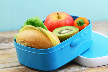 Packed lunch containing cheese roll, crunchy yellow pepper and fresh fruit: red apple and kiwi fruit
