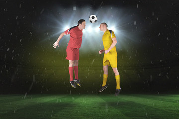 Naklejka premium Football players tackling for the ball against football pitch under spotlights