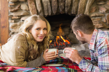 Couple with tea cups in front of lit fireplace