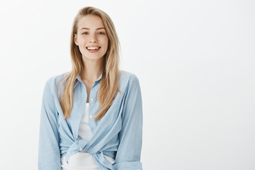 Portrait of kind charming european female student in stylish outfit, smiling friendly and happilly...