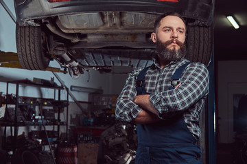Obraz na płótnie Canvas Two bearded brutal mechanics repair a car on a lift in the garage. 