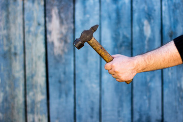 Man's hand holds a hammer on an old wooden blue background