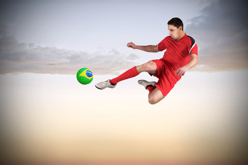 Naklejka premium Fit football player jumping and kicking against beautiful orange and blue sky