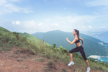 Naklejka na ściany i meble Slender young female athlete doing cardio exercise going up the mountain with sea in background.