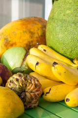 Tropical exotic fruits on a green wooden background.  Custard apple, bananas, lady finger, banana, papaya, mango, longan, lam-yai, rambutan, rambutans.