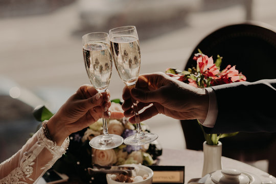 Romantic couple have dinner together in cafe or restaurant, clink glasses of champagne, beautiful bouquets in background. People, celebration and holidays concept