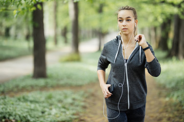 Running woman. Female Runner Jogging during Outdoor Workout in a Park with music on headphone from phone.