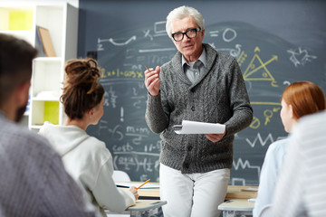 Confident mature teacher answering questions of his students after explanation of subject