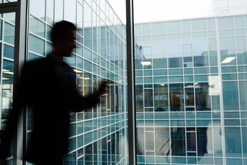 Fototapeta na wymiar Blurry silhouette of businessman in motion along large window of contemporary office center