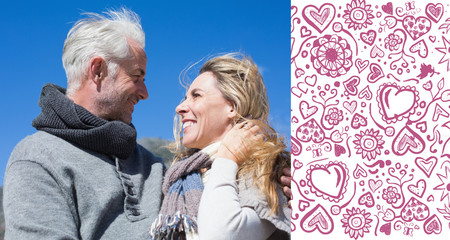 Carefree couple hugging in warm clothing against valentines pattern