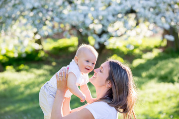 Happy mom, holding her cute baby boy in spring park