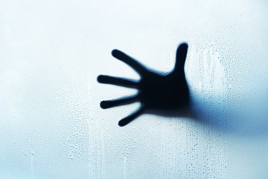 Blue hand silhouette behind a glass with water drops