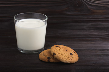 Oatmeal cookies with chocolate and a glass of milk on a brown wooden table