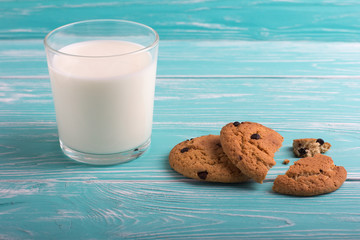 Broken oatmeal cookies with chocolate and a glass of milk on a blue wooden table