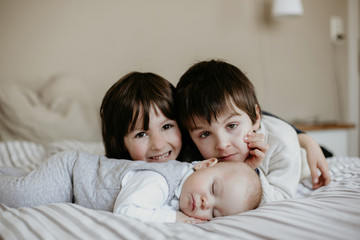 Little baby boy, sleeping in big bed in the afternoon, brothers kissing and hugging him