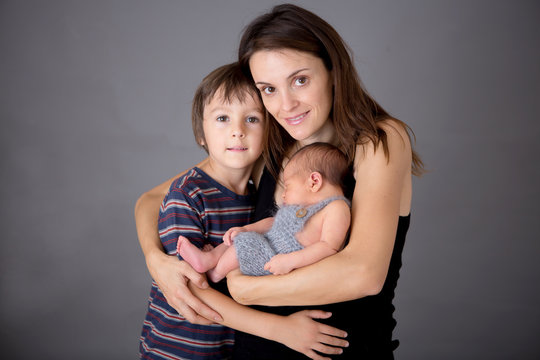 Family picture of two boys and their mom, kissing and hugging newborn baby