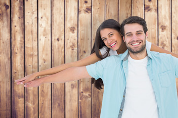 Happy casual man giving pretty girlfriend piggy back against wooden planks