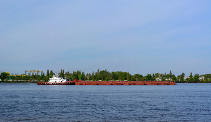 The tug pushes the barge along the river against the background of the forest and the blue sky. Copy space.