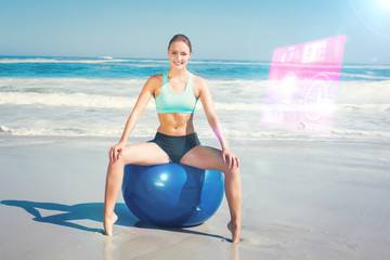 Fit woman sitting on exercise ball at the beach against fitness interface