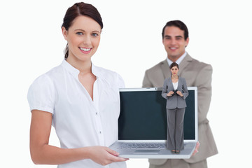 Young businesswoman with binoculars against smiling saleswoman presenting laptop screen with colleague behind her