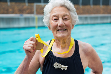 Senior woman showing gold medal at poolside