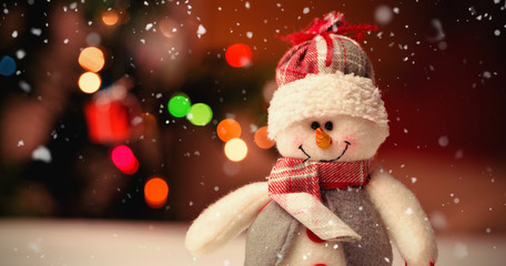 Snow falling against close-up of snowman on wooden table