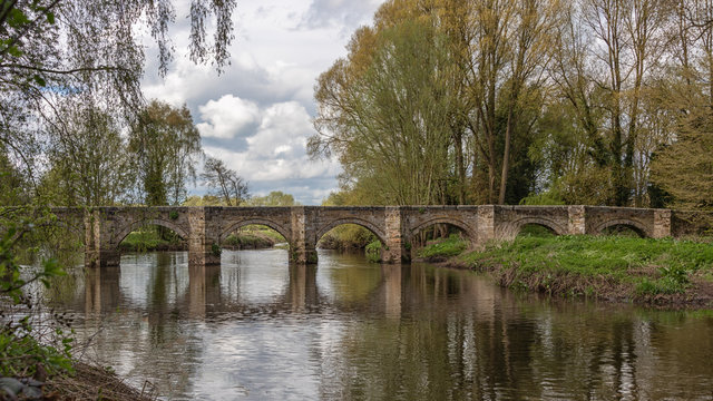 a landscape photograph of a long packhorse bridge made of stone and spanning the river trent