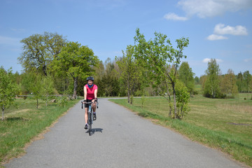 Fototapeta premium Happy young girl on bike riding through the nice landscape during beautiful spring day 