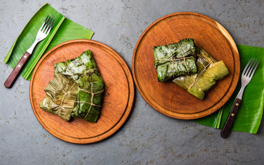 COLOMBIAN, CENTRAL AMERICAN FOOD. Tamales wrapped in banana palm tree leaves on wooden plates, gray stone background