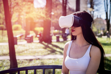 Virtual reality, fun in the park. A woman relaxes in the park using googles VR. The girl imagines that she is climbing the rope. Spending free time outside, lifestyle concept.