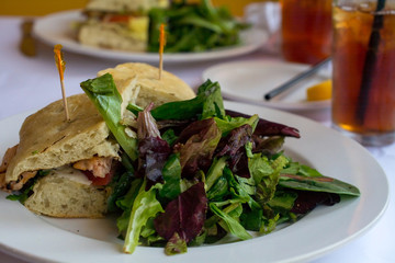 Salad and grilled Salmon sandwich in ciabatta bread  in a restaurant setting with ice tea 