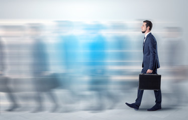 Young businessman with briefcase hurry up on a crowded street with blurred people around
