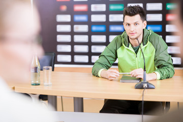 Portrait of young professional sportsman speaking to microphone at press conference, copy space